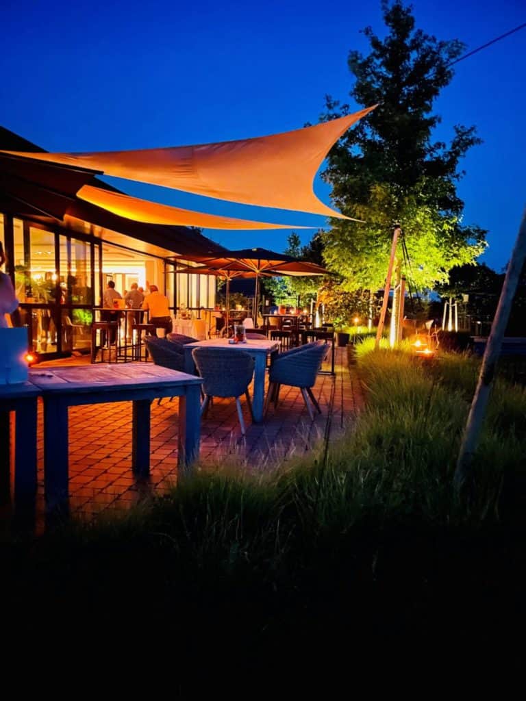 Een restaurant met 's avonds buitentafels en stoelen, waardoor er een gezellige en sfeervolle ambiance ontstaat.